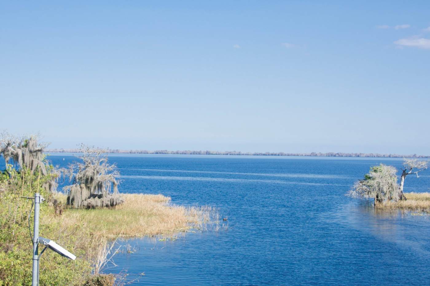 A serene landscape featuring a deep blue body of water with small patches of land and palm trees under a clear blue sky.